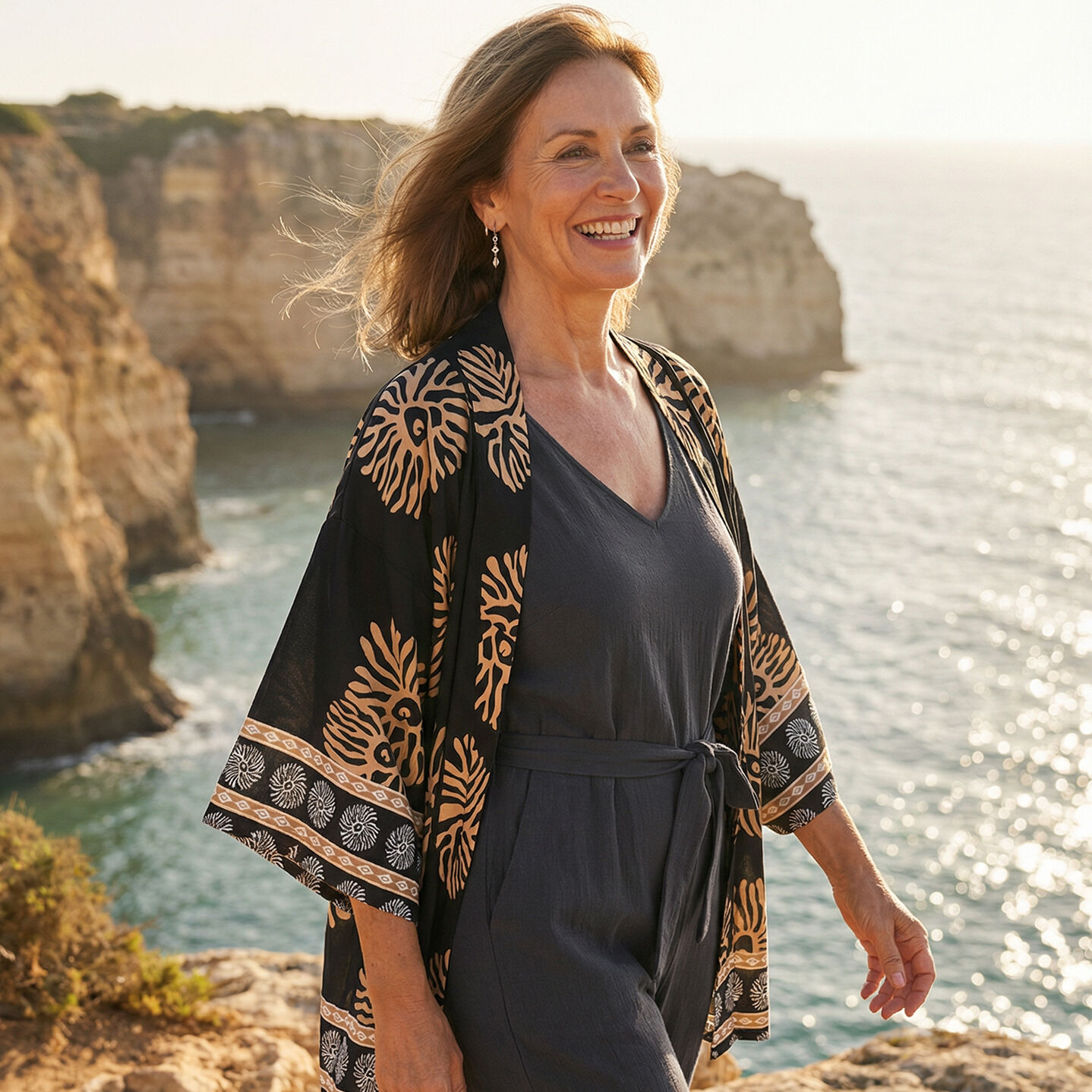 Woman on cliff with wind in her hair. Printed kimono. Smiling
