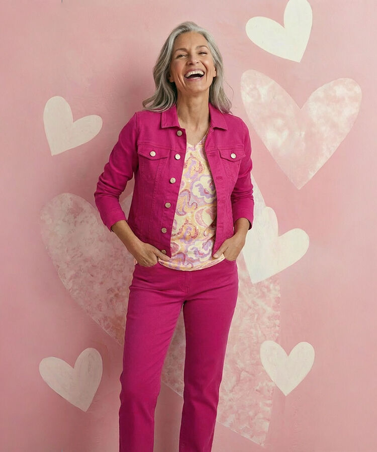Smiling with laughter woman wearing fuchsia jean jacket and matching pant. Heart textured wall paper.